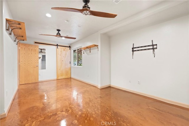 spare room featuring ceiling fan, a barn door, and concrete flooring