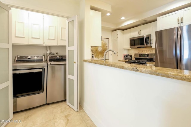 kitchen featuring light tile patterned floors, white cabinetry, stainless steel appliances, separate washer and dryer, and light stone counters