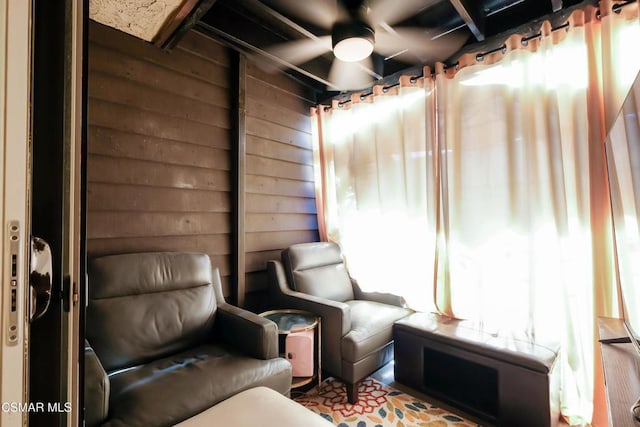 living area with ceiling fan and wood walls