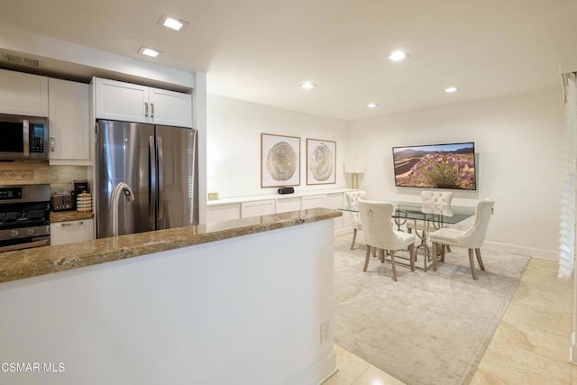 kitchen featuring stainless steel appliances, backsplash, white cabinets, and light stone countertops