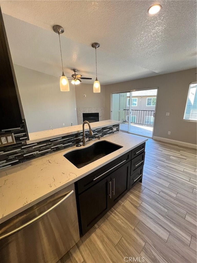 kitchen with pendant lighting, sink, dishwasher, light stone counters, and a fireplace