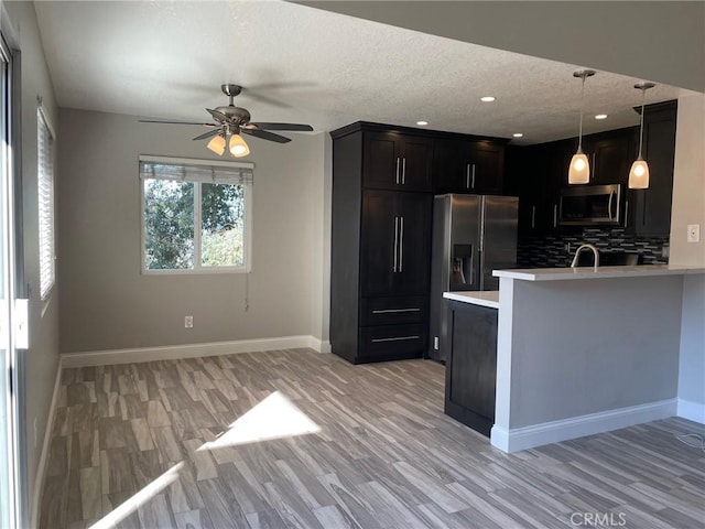 kitchen featuring appliances with stainless steel finishes, decorative light fixtures, kitchen peninsula, and light hardwood / wood-style flooring