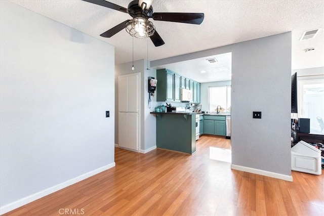 kitchen with ceiling fan, a textured ceiling, appliances with stainless steel finishes, and light hardwood / wood-style flooring