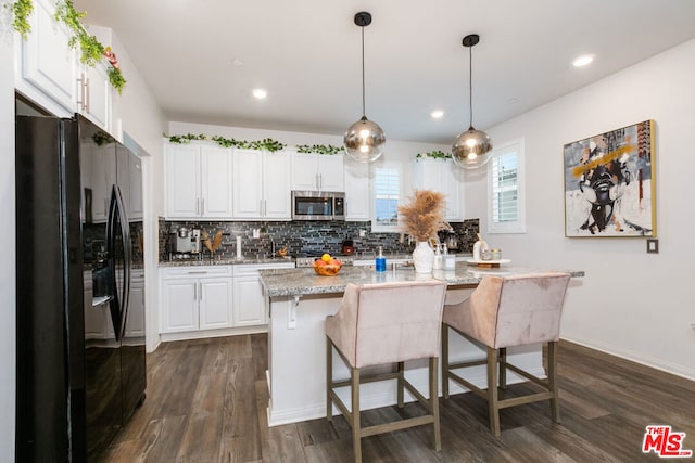 kitchen with decorative light fixtures, white cabinetry, an island with sink, black fridge, and light stone counters