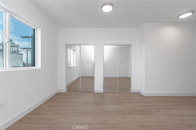 unfurnished bedroom with light hardwood / wood-style floors and two closets