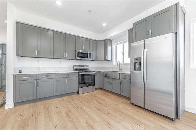 kitchen with sink, appliances with stainless steel finishes, gray cabinetry, and light wood-type flooring