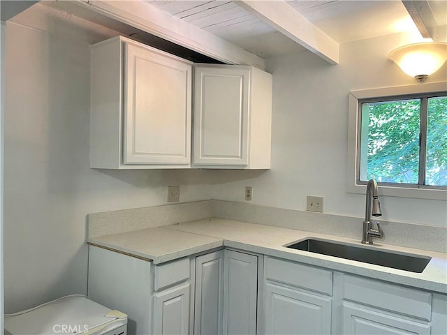 kitchen featuring light stone counters, sink, white cabinets, and beam ceiling