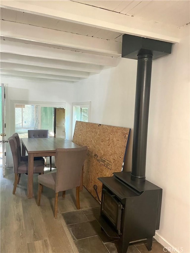 dining space featuring dark wood-type flooring, beamed ceiling, and a wood stove