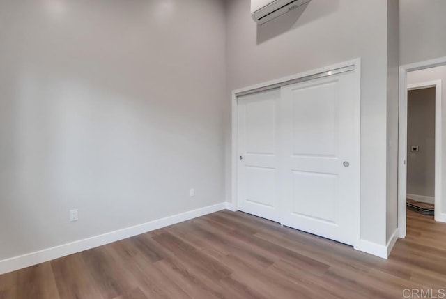 unfurnished bedroom with a closet, a wall unit AC, and wood-type flooring