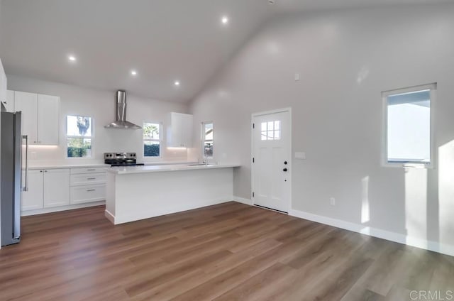 kitchen with wood-type flooring, appliances with stainless steel finishes, white cabinets, high vaulted ceiling, and wall chimney range hood