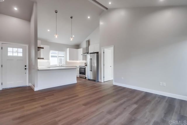 kitchen featuring beamed ceiling, hanging light fixtures, white cabinets, stainless steel appliances, and wall chimney exhaust hood