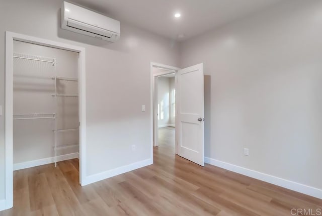 unfurnished bedroom featuring a closet, a wall mounted AC, and light hardwood / wood-style flooring