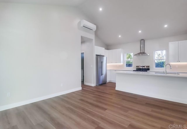 kitchen featuring wall chimney exhaust hood, white cabinets, a wall unit AC, and appliances with stainless steel finishes