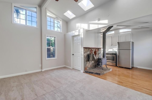 interior space with light carpet, white cabinets, a wood stove, beamed ceiling, and stainless steel appliances