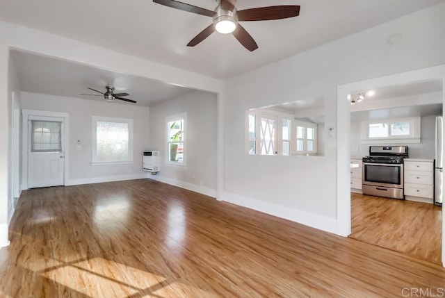 unfurnished living room with light hardwood / wood-style floors, heating unit, and ceiling fan