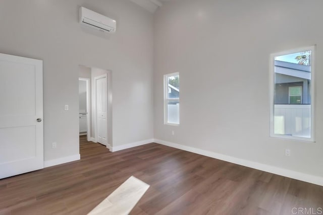 empty room featuring a high ceiling, dark hardwood / wood-style flooring, and a wall mounted air conditioner