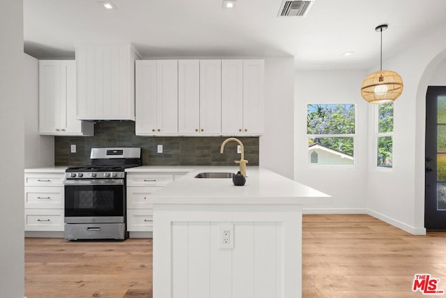 kitchen with white cabinets, stainless steel range oven, decorative light fixtures, sink, and backsplash