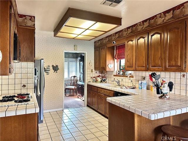 kitchen featuring light tile patterned floors, tile countertops, kitchen peninsula, stainless steel fridge, and sink