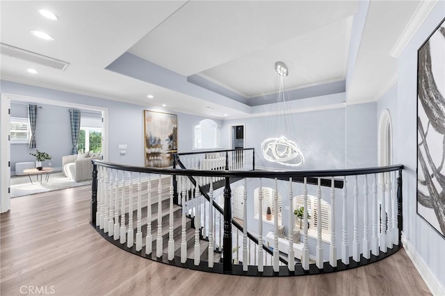 corridor with hardwood / wood-style floors, a tray ceiling, crown molding, and a chandelier