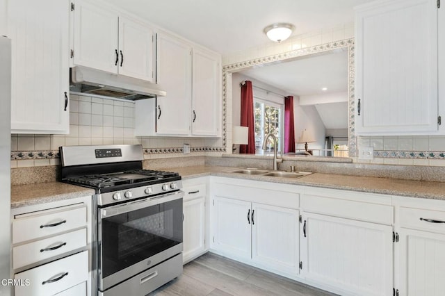 kitchen featuring stainless steel gas range, backsplash, white cabinets, and sink