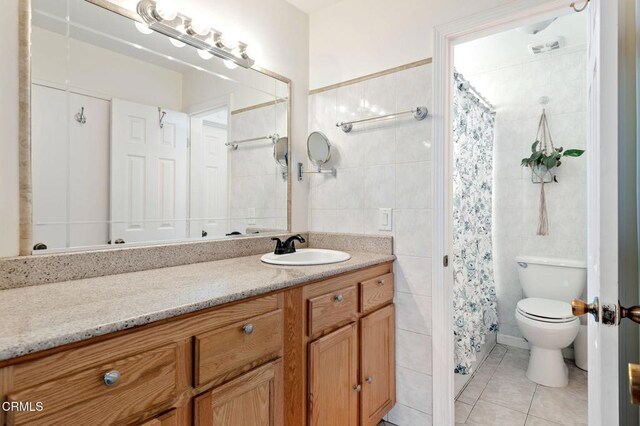 bathroom with toilet, vanity, tile walls, tile patterned floors, and curtained shower