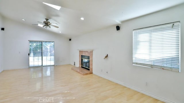 unfurnished living room with ceiling fan, a tiled fireplace, vaulted ceiling, and light hardwood / wood-style floors