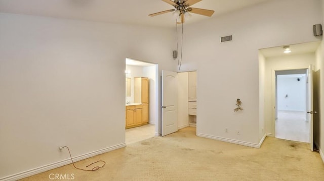 unfurnished bedroom with ceiling fan, light carpet, a towering ceiling, and connected bathroom