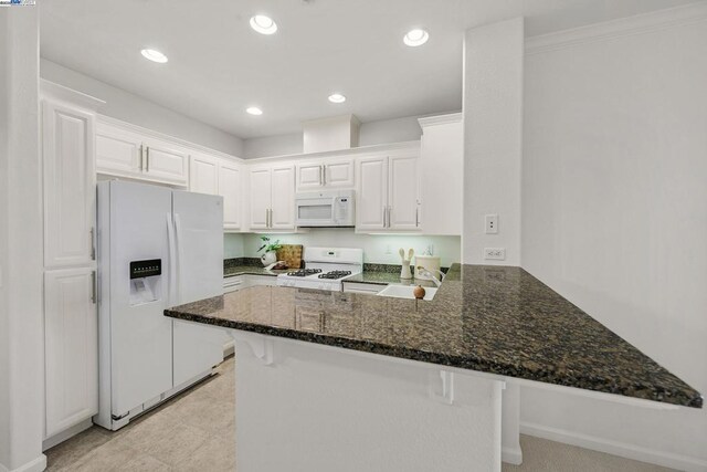 kitchen with kitchen peninsula, dark stone countertops, white appliances, and white cabinetry