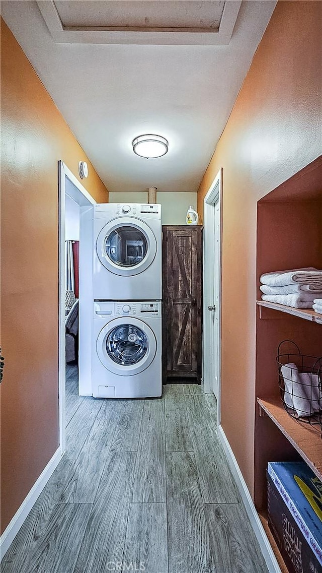 clothes washing area with wood-type flooring and stacked washer / dryer