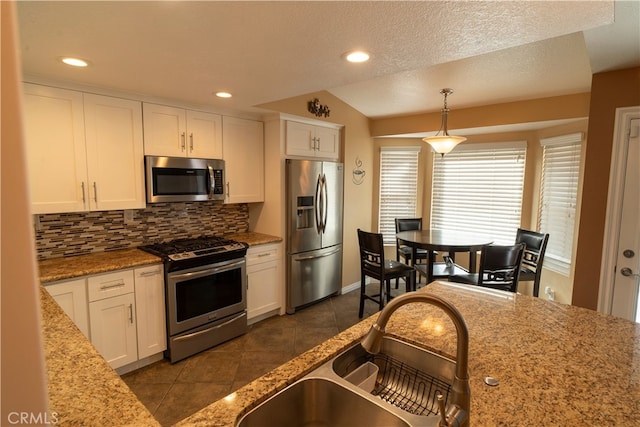 kitchen with stainless steel appliances, sink, white cabinets, backsplash, and pendant lighting