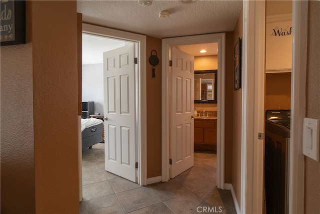 hall with a textured ceiling, washer / clothes dryer, sink, and light tile patterned floors