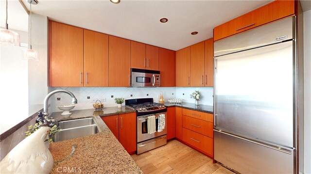 kitchen with backsplash, stone counters, light hardwood / wood-style floors, sink, and appliances with stainless steel finishes