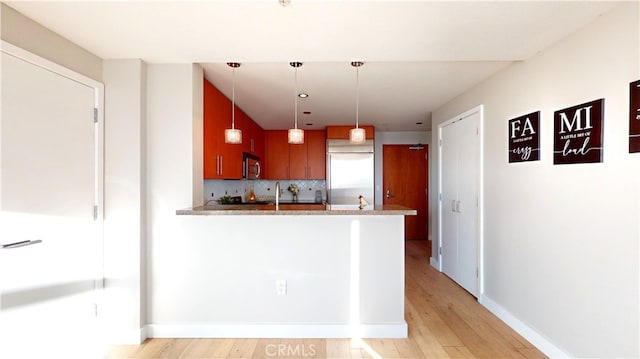 kitchen featuring light stone countertops, pendant lighting, appliances with stainless steel finishes, decorative backsplash, and kitchen peninsula