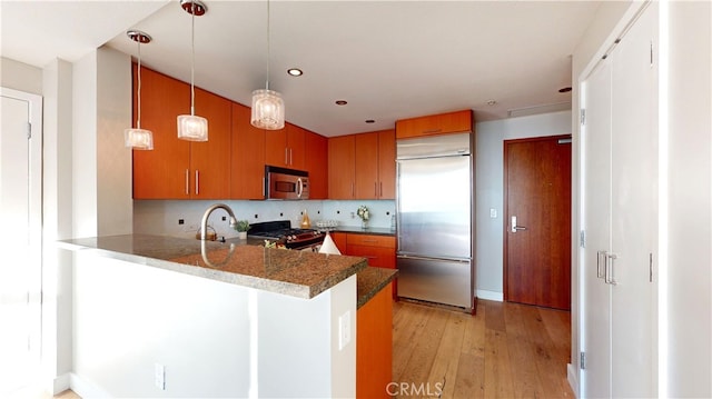 kitchen with pendant lighting, stainless steel appliances, decorative backsplash, kitchen peninsula, and light wood-type flooring