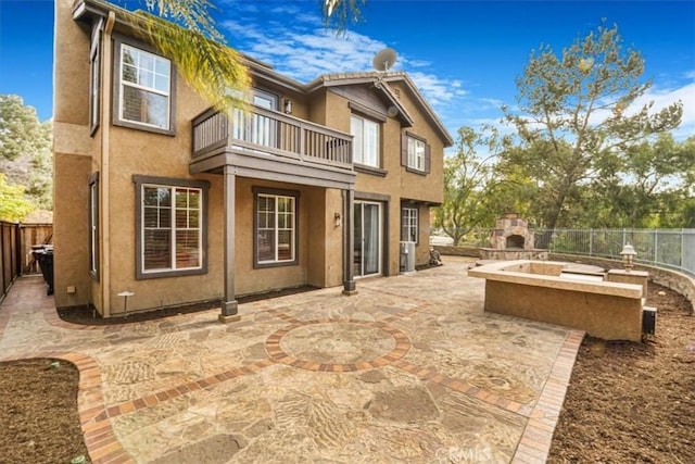 rear view of house with a patio, a balcony, and exterior fireplace