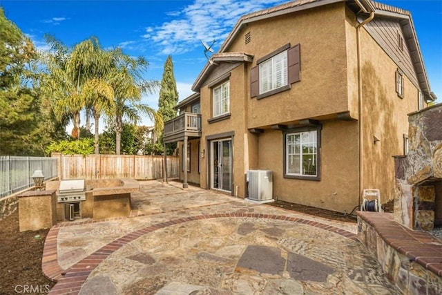 back of house with a balcony, a patio area, cooling unit, and exterior kitchen