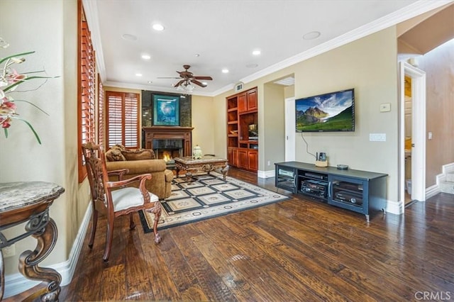 living room featuring ceiling fan, dark hardwood / wood-style flooring, ornamental molding, and a large fireplace