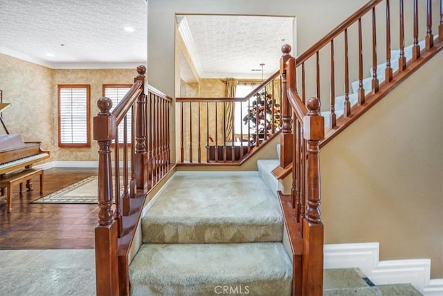 staircase with a textured ceiling, ornamental molding, and wood-type flooring