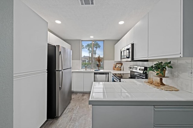 kitchen featuring white cabinetry, kitchen peninsula, stainless steel appliances, backsplash, and light hardwood / wood-style flooring