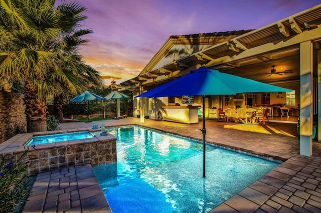 pool at dusk featuring exterior kitchen, a patio, and an in ground hot tub