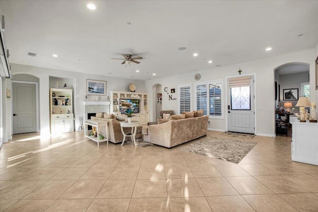 living room with ceiling fan, built in shelves, light tile patterned flooring, and a stone fireplace