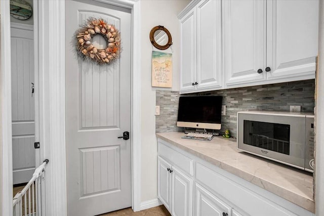 bar with decorative backsplash, light stone countertops, and white cabinetry