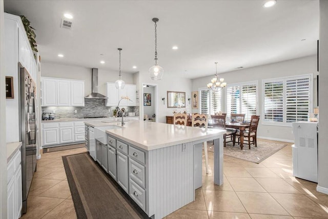 kitchen with white cabinetry, a center island with sink, hanging light fixtures, and wall chimney range hood