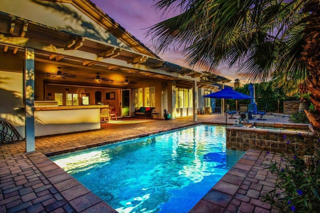 pool at dusk featuring ceiling fan, exterior bar, a patio, and an in ground hot tub