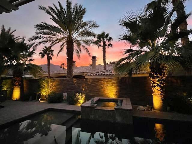 pool at dusk featuring a patio area and an in ground hot tub