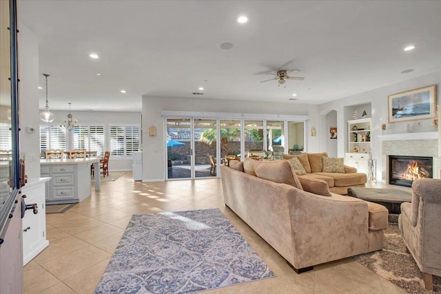 tiled living room with ceiling fan with notable chandelier and built in features