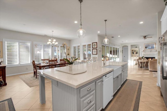 kitchen featuring ceiling fan with notable chandelier, pendant lighting, dishwasher, sink, and a kitchen island with sink