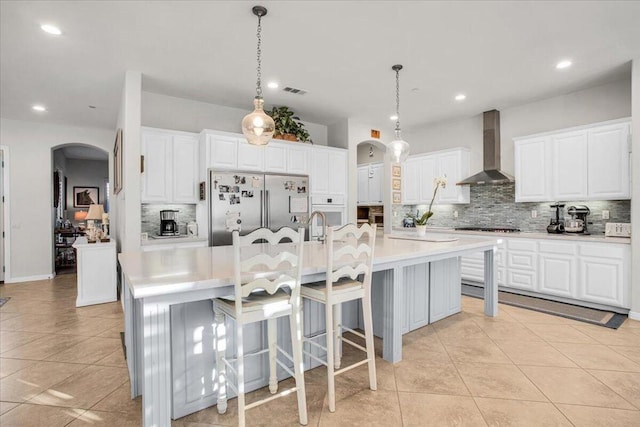 kitchen featuring pendant lighting, white cabinets, a large island with sink, wall chimney exhaust hood, and stainless steel fridge