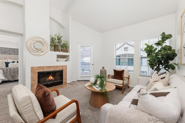 living room featuring a tile fireplace, vaulted ceiling, and carpet flooring