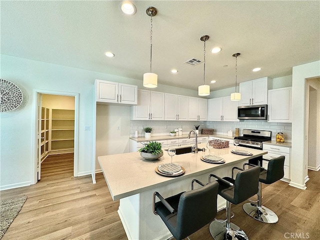 kitchen with stainless steel appliances, sink, white cabinetry, and an island with sink